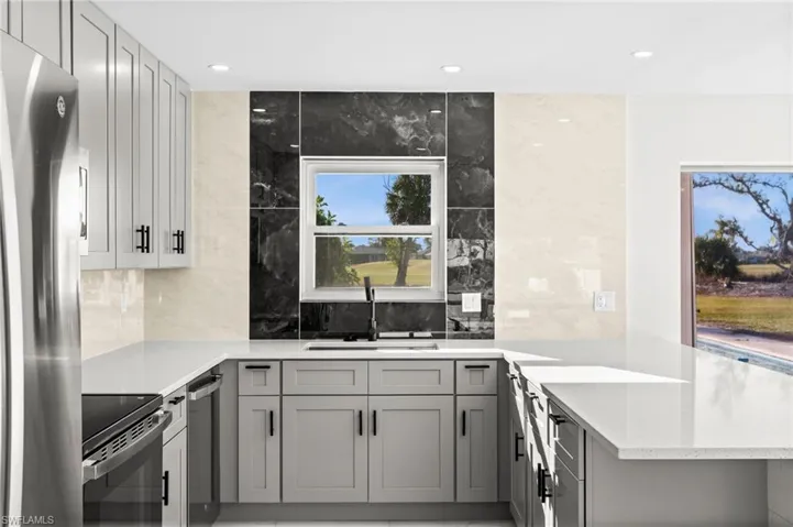 Kitchen featuring gray cabinetry, a peninsula, light stone counters, stainless steel appliances, and recessed lighting