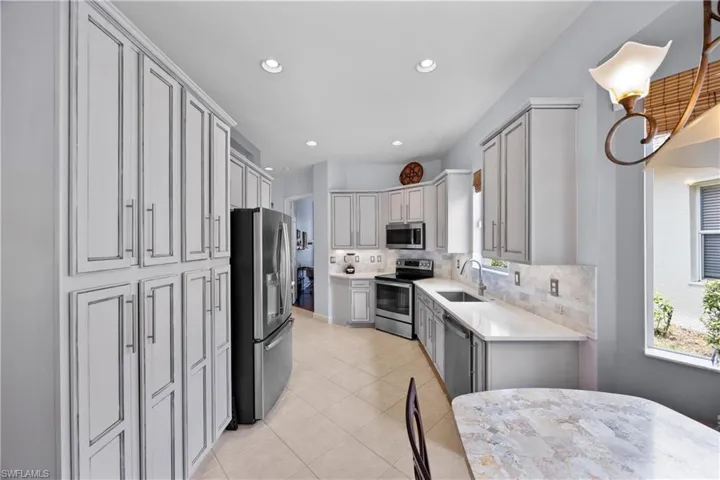 Kitchen featuring decorative backsplash, appliances with stainless steel finishes, light tile patterned flooring, custom cabinets, and sink