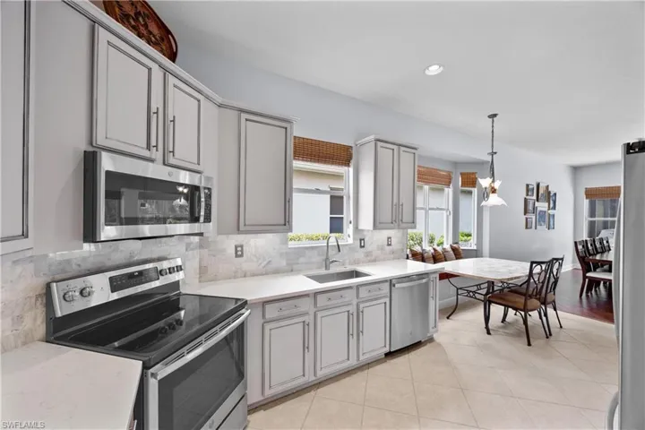 Kitchen with hanging light fixtures, appliances with stainless steel finishes, gray cabinets, sink, and tile flooring on the diagonal