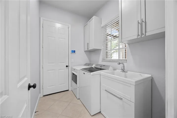 Laundry room featuring cabinets, washing machine and dryer, light tile patterned floors, and sink