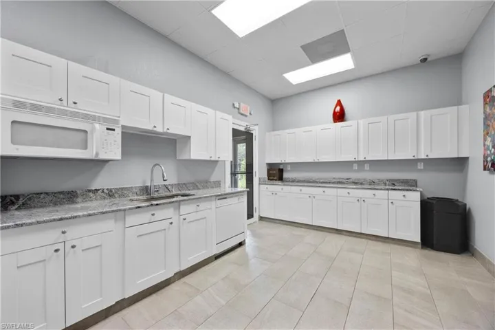 Kitchen featuring white appliances, sink, light tile patterned flooring, and white cabinetry
