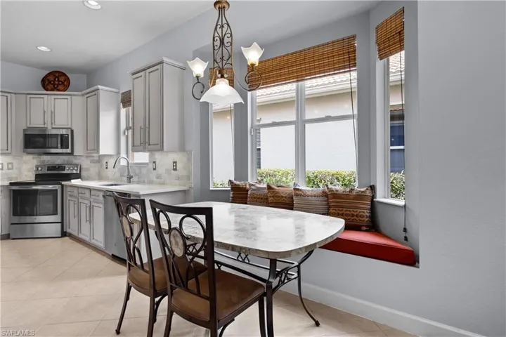 Kitchen with stainless steel appliances, light tile patterned floors, hanging light fixtures, decorative backsplash, and gray cabinetry