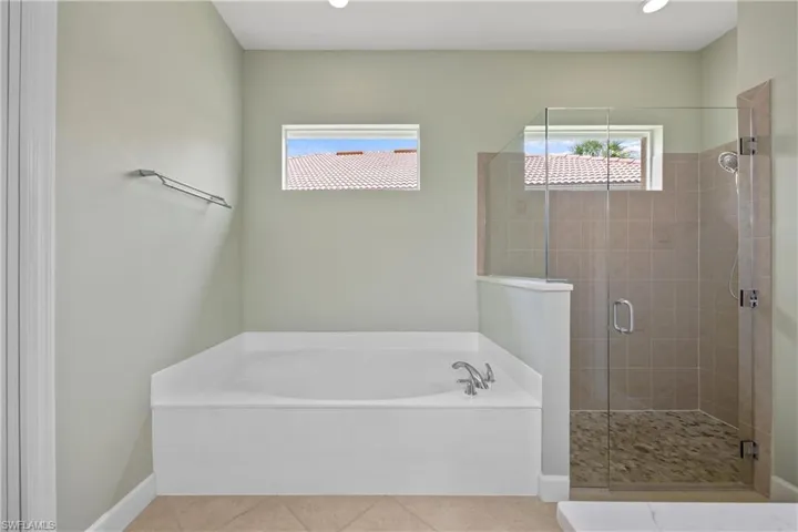Primary bathroom with shower with separate bathtub and tile patterned flooring