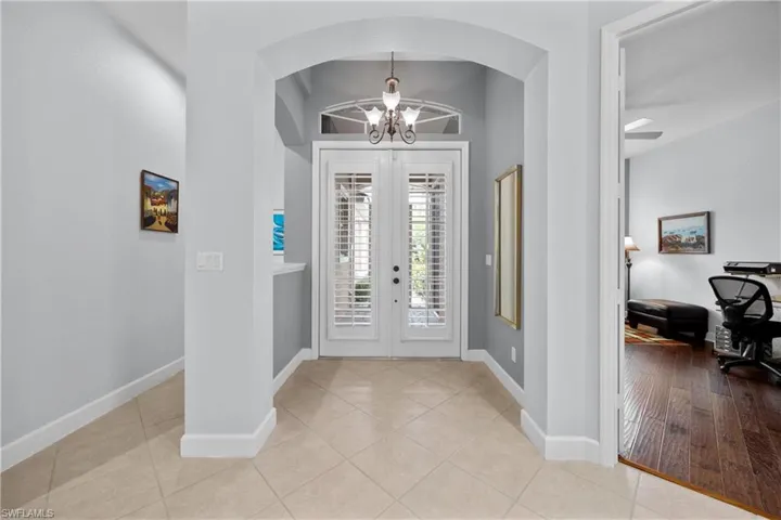Tiled entrance foyer with ceiling fan with notable chandelier, french doors, and lofted ceiling