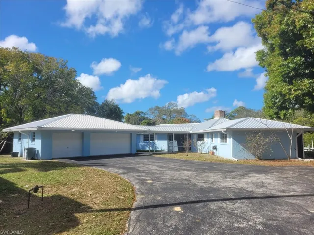 Single story home with driveway, an attached garage, a metal roof, a front lawn, and stucco siding