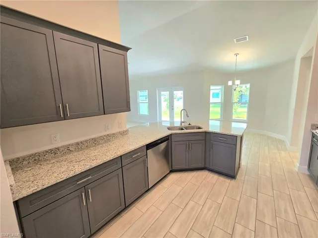 Kitchen featuring kitchen peninsula, sink, stainless steel dishwasher, and light stone counters