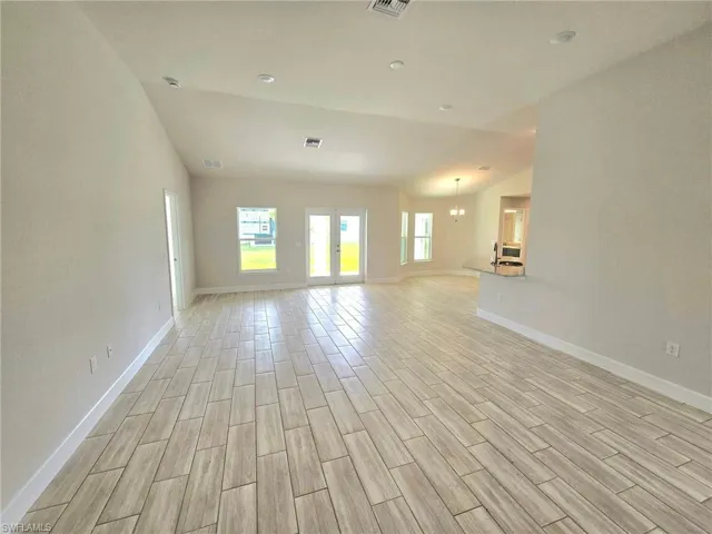 Unfurnished living room with lofted ceiling, light wood-type flooring, and an inviting chandelier