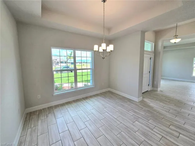 Spare room with a raised ceiling, light hardwood / wood-style flooring, and a chandelier