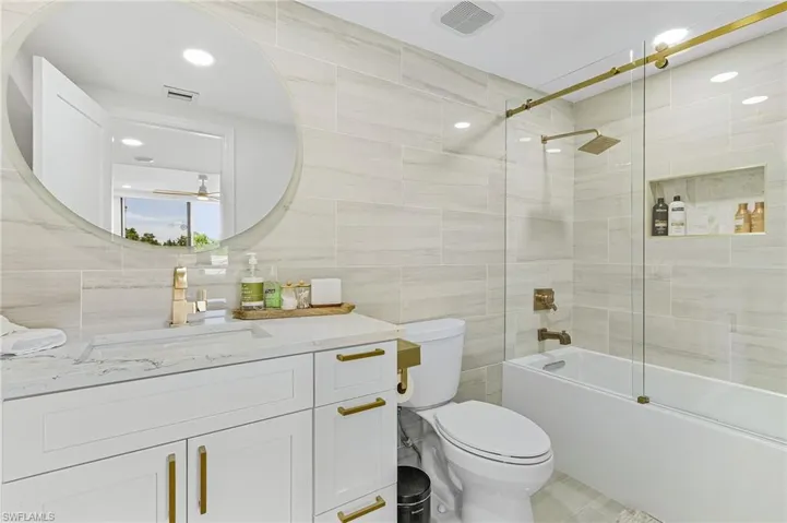 Full bathroom with tile walls, toilet, enclosed tub / shower combo, and vanity
