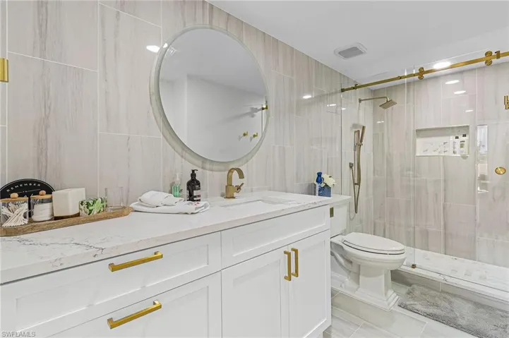 Bathroom featuring tiled shower, toilet, vanity, tile walls, and tile patterned floors