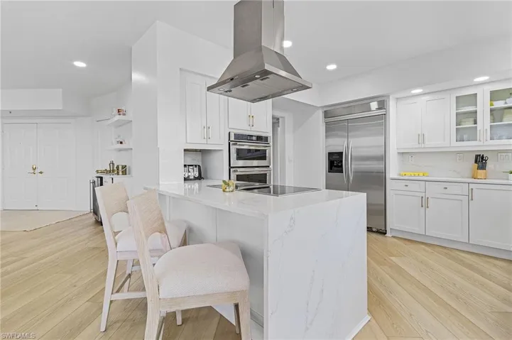 Kitchen featuring appliances with stainless steel finishes, light hardwood / wood-style flooring, light stone counters, island exhaust hood, and white cabinetry