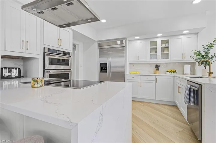 Kitchen with white cabinetry, sink, exhaust hood, light hardwood / wood-style floors, and appliances with stainless steel finishes