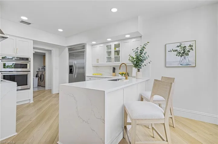 Kitchen with white cabinetry, light stone counters, stainless steel appliances, light hardwood / wood-style floors, and sink