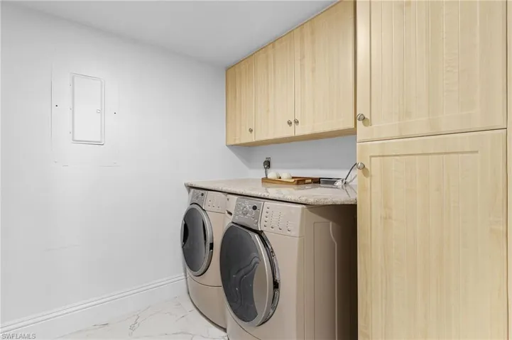 Clothes washing area with light tile patterned flooring, washing machine and clothes dryer, electric panel, and cabinets