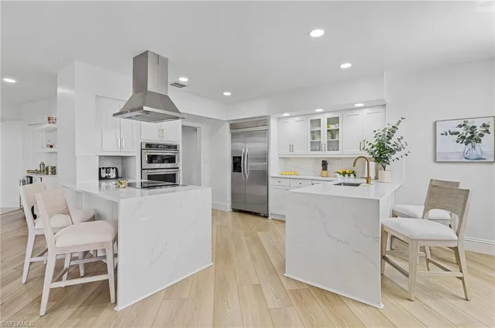 Kitchen featuring white cabinetry, light wood-type flooring, sink, island exhaust hood, and appliances with stainless steel finishes