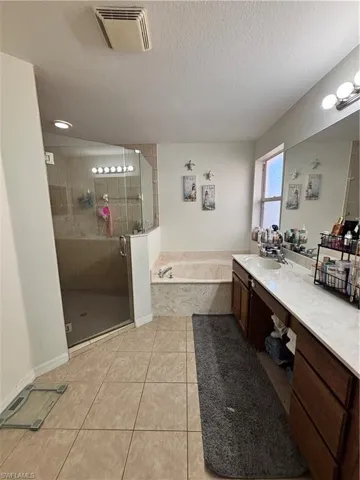 Full bathroom with a shower stall, vanity, a bath, a textured ceiling, and light tile patterned flooring
