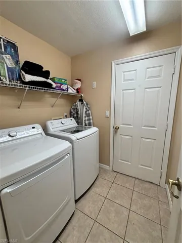 Laundry area with a textured ceiling, light tile patterned floors, and independent washer and dryer