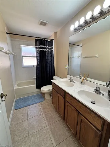 Bathroom featuring double vanity, shower / bath combo with shower curtain, and light tile patterned floors