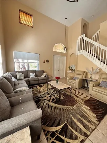 Tiled living room with stairway and a high ceiling
