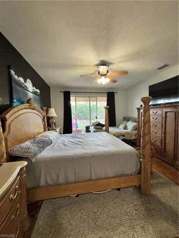 Bedroom with a textured ceiling, ceiling fan, access to exterior, and dark wood finished floors