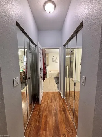 Hallway featuring a textured wall, wood finished floors, and a textured ceiling