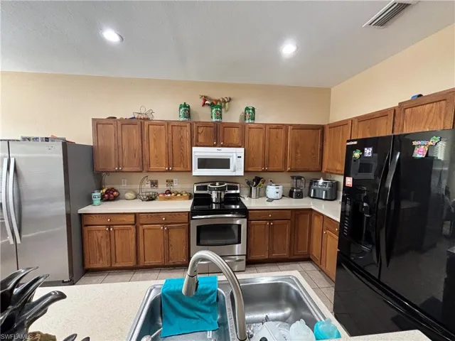 Kitchen featuring wood finish cabinets, stainless steel appliances, light countertops, light tile patterned floors, and recessed lighting