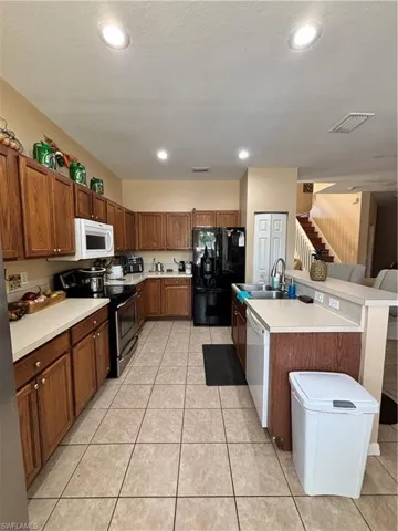 Kitchen with light countertops, stove, black refrigerator, a center island with sink, and wood finish cabinets