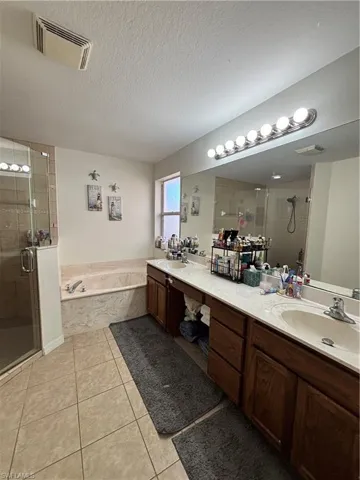 Bathroom with a stall shower, double vanity, light tile patterned floors, a bath, and a textured ceiling