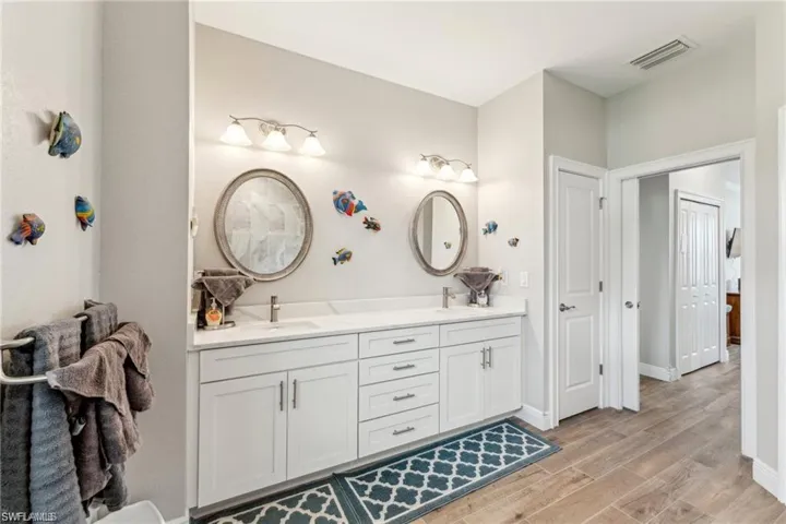 Bathroom with a sink, wood finished floors, baseboards, visible vents, and double vanity