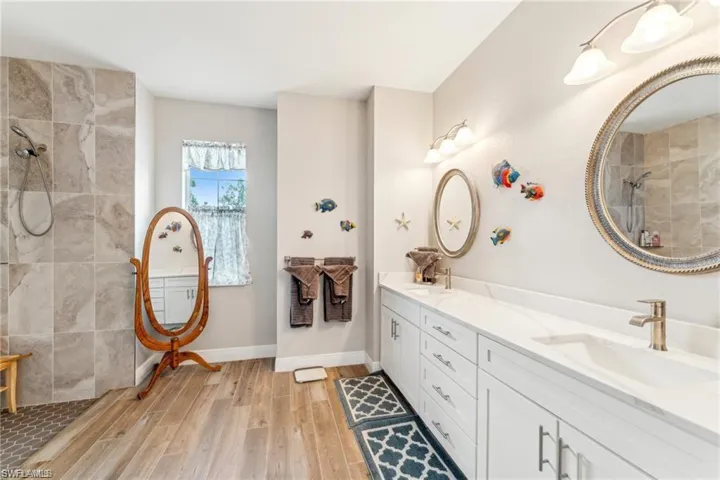 Full bathroom featuring a sink, wood finished floors, walk in shower, baseboards, and double vanity
