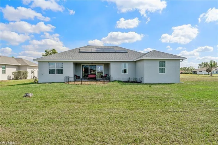 Back of house with stucco siding, a shingled roof, roof mounted solar panels, and a yard