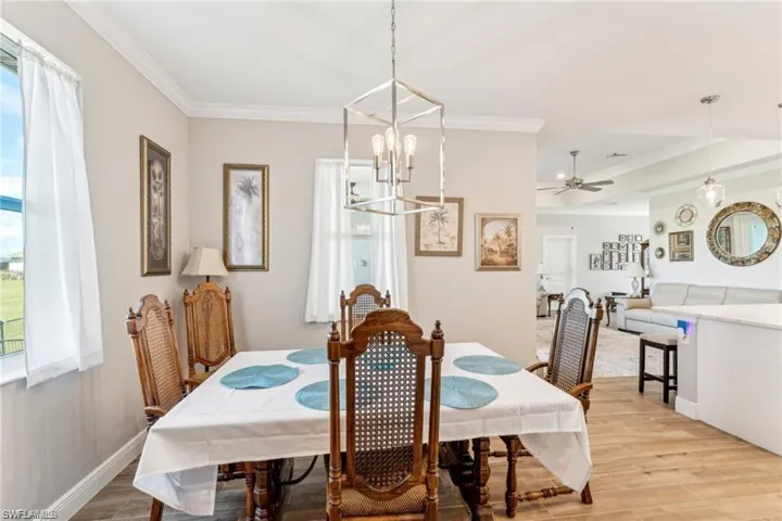 Dining room featuring ornamental molding, ceiling fan with notable chandelier, baseboards, and light wood-type flooring