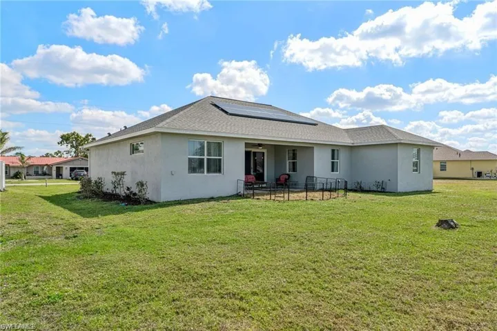 Rear view of house featuring a patio, stucco siding, a yard, and roof mounted solar panels