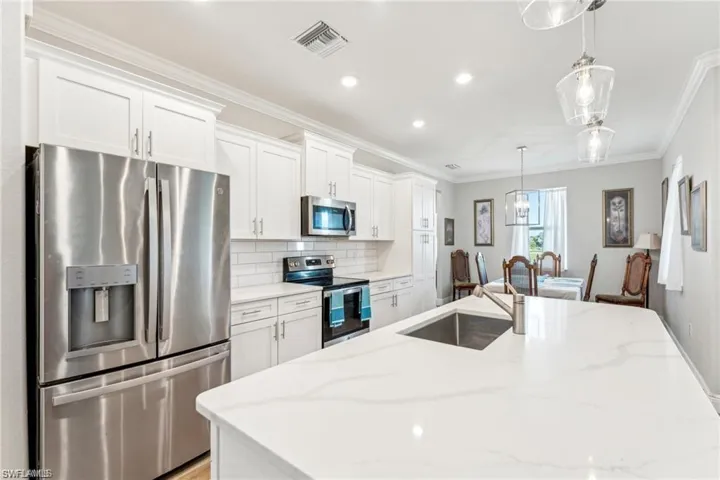 Kitchen featuring crown molding, a sink, appliances with stainless steel finishes, visible vents, and white cabinets
