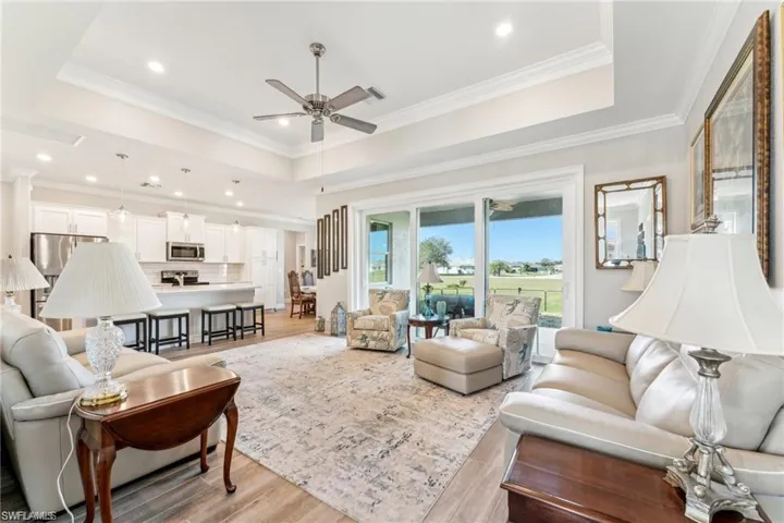 Living room with a tray ceiling, light wood finished floors, crown molding, and a ceiling fan