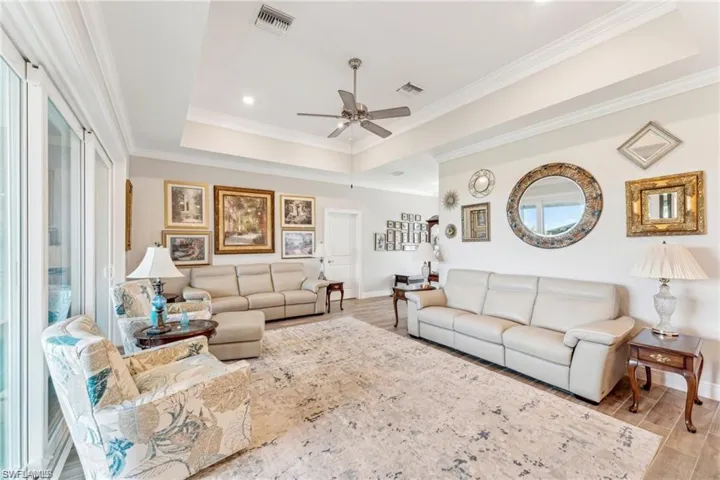 Living area featuring a raised ceiling, wood finished floors, ceiling fan, and visible vents