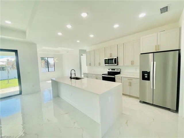 Kitchen featuring appliances with stainless steel finishes, light marble finish flooring, recessed lighting, light stone counters, and a kitchen island with sink