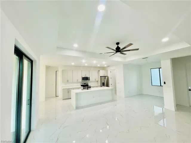 Kitchen with a tray ceiling, open floor plan, a center island with sink, recessed lighting, and white cabinetry