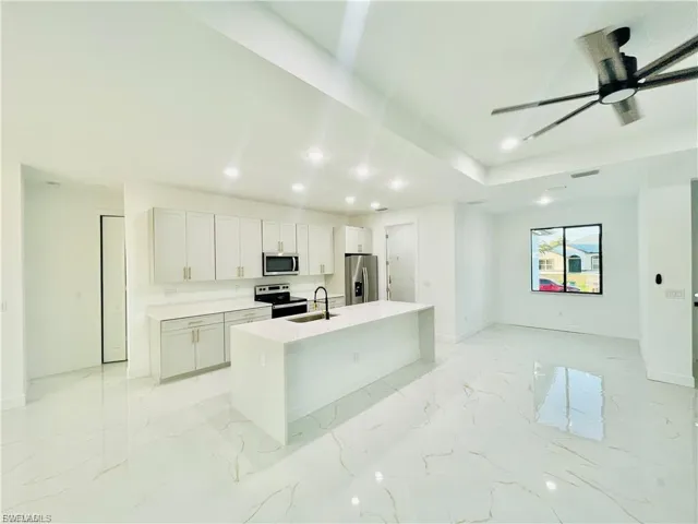 Kitchen with an island with sink, appliances with stainless steel finishes, white cabinetry, light marble finish floors, and recessed lighting