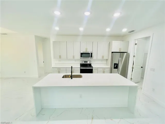 Kitchen with light stone countertops, appliances with stainless steel finishes, a center island with sink, light marble finish floors, and recessed lighting