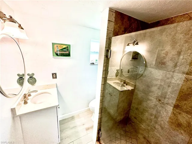 Bathroom with vanity, a textured ceiling, toilet, and a shower with door