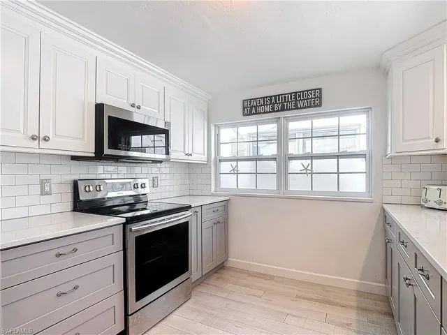 Kitchen featuring light hardwood / wood-style flooring, decorative backsplash, white cabinetry, and appliances with stainless steel finishes