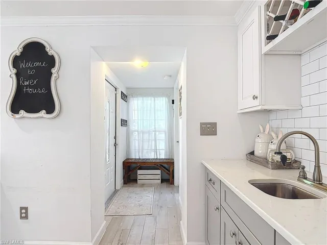 Kitchen featuring light wood-type flooring, backsplash, sink, and light stone counters