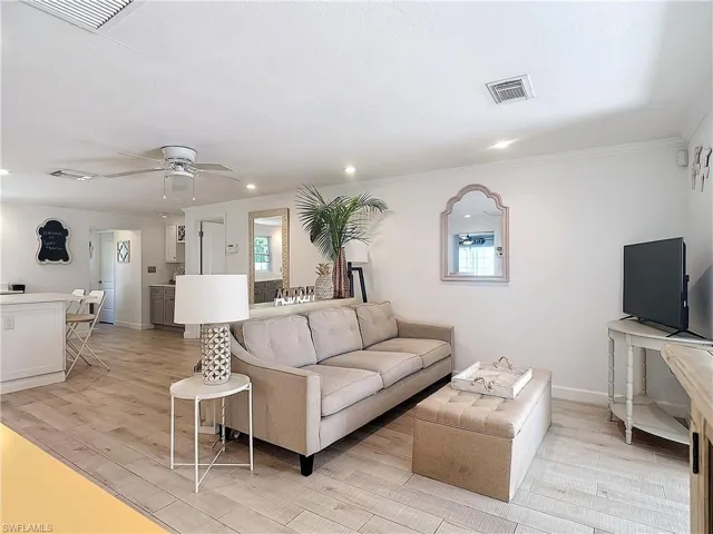 Living room with crown molding, light wood-type flooring, ceiling fan, and plenty of natural light