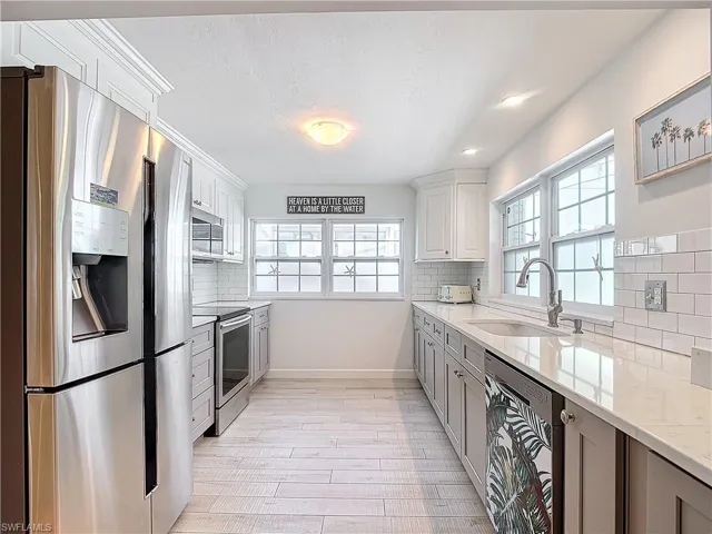 Kitchen featuring light stone counters, tasteful backsplash, white cabinets, stainless steel appliances, and sink