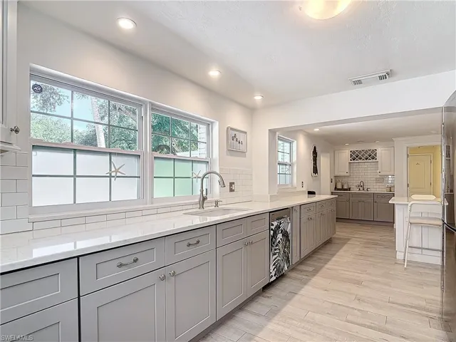 Kitchen with gray cabinets, light hardwood / wood-style floors, tasteful backsplash, and sink