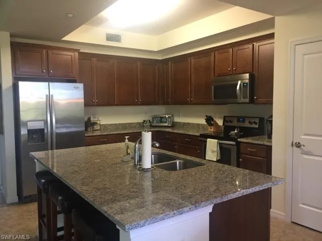 Kitchen featuring stainless steel appliances, dark stone counters, a kitchen breakfast bar, dark brown cabinets, and an island with sink