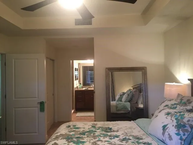 Bedroom featuring a ceiling fan, a tray ceiling, and connected bathroom