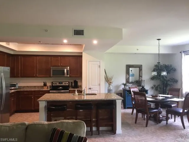Kitchen with light stone counters, appliances with stainless steel finishes, a kitchen island with sink, a breakfast bar area, and decorative light fixtures