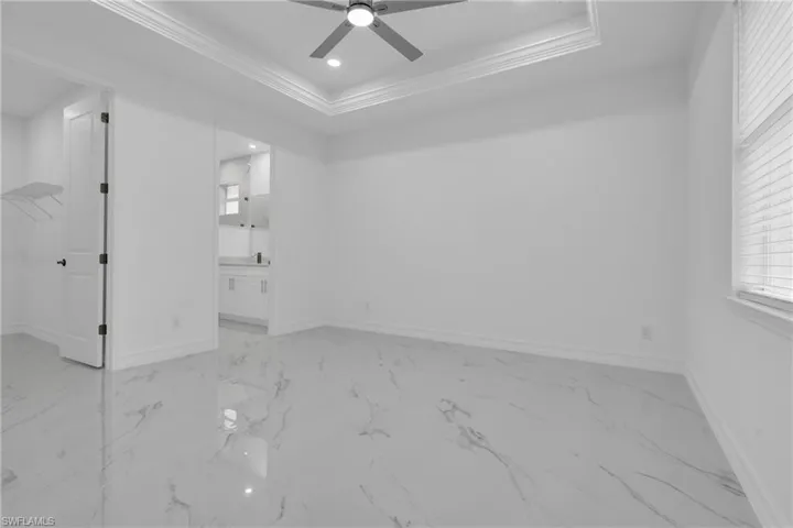 Spare room with a raised ceiling, recessed lighting, light marble finish flooring, a ceiling fan, and ornamental molding